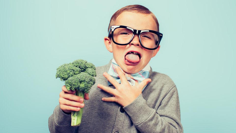 Kleiner Junge mit Brille ekelt sich vor einem Brokkoli, den er in der Hand hält