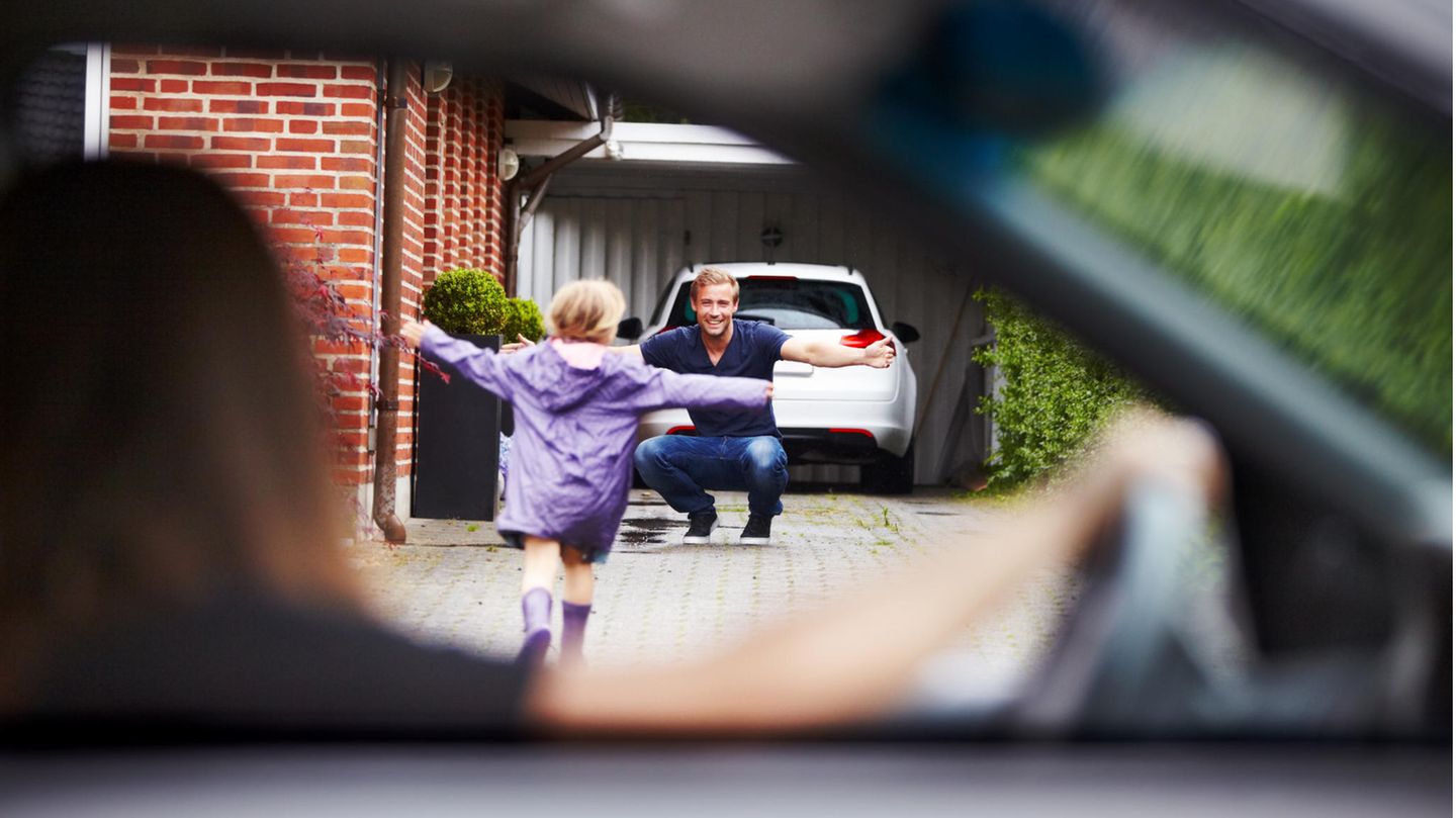 Kind läuft dem Vater in die Arme und die Mutter beobachtet das aus dem Auto heraus