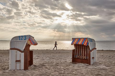 Eine Frau joggt am Strand entlang. Im Vordergrund sind zwei Strandkörbe zu sehen.