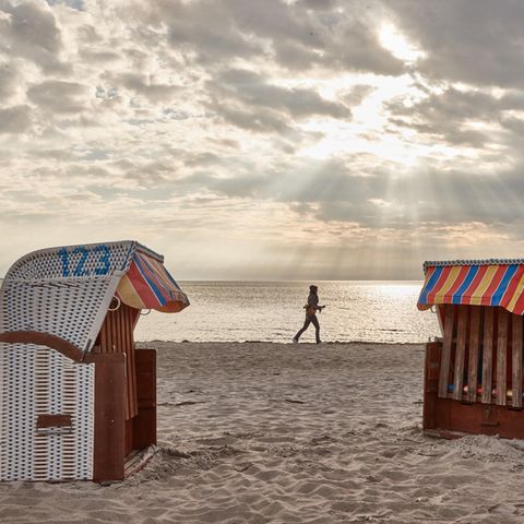 Eine Frau joggt am Strand entlang. Im Vordergrund sind zwei Strandkörbe zu sehen.