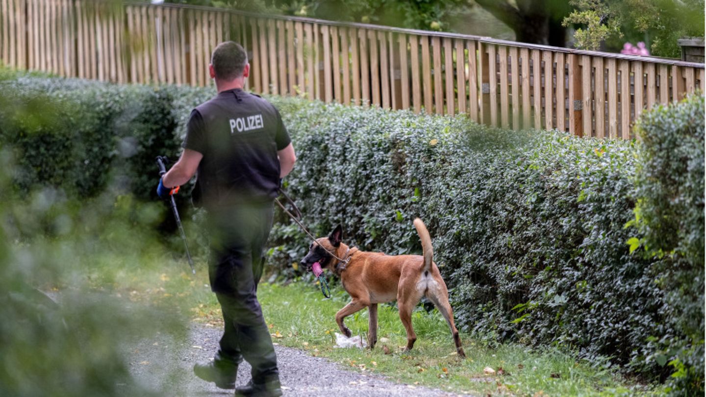 Ein Polizeibeamter mit einem Hund durchsucht eine Kleingarten-Parzelle