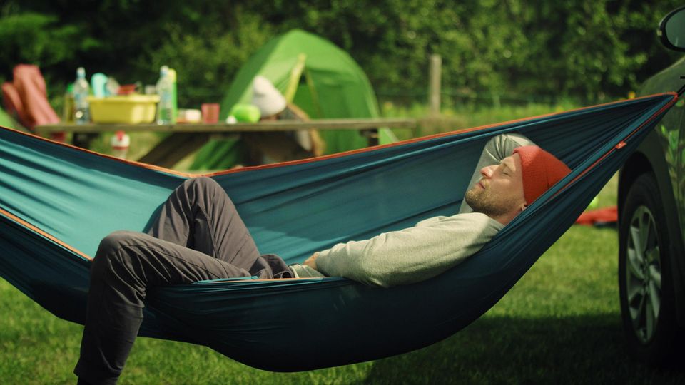 Outdoor Hängematte: Junger Mann schläft auf einem Zeltplatz in der Hängematte