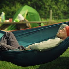 Outdoor Hängematte: Junger Mann schläft auf einem Zeltplatz in der Hängematte