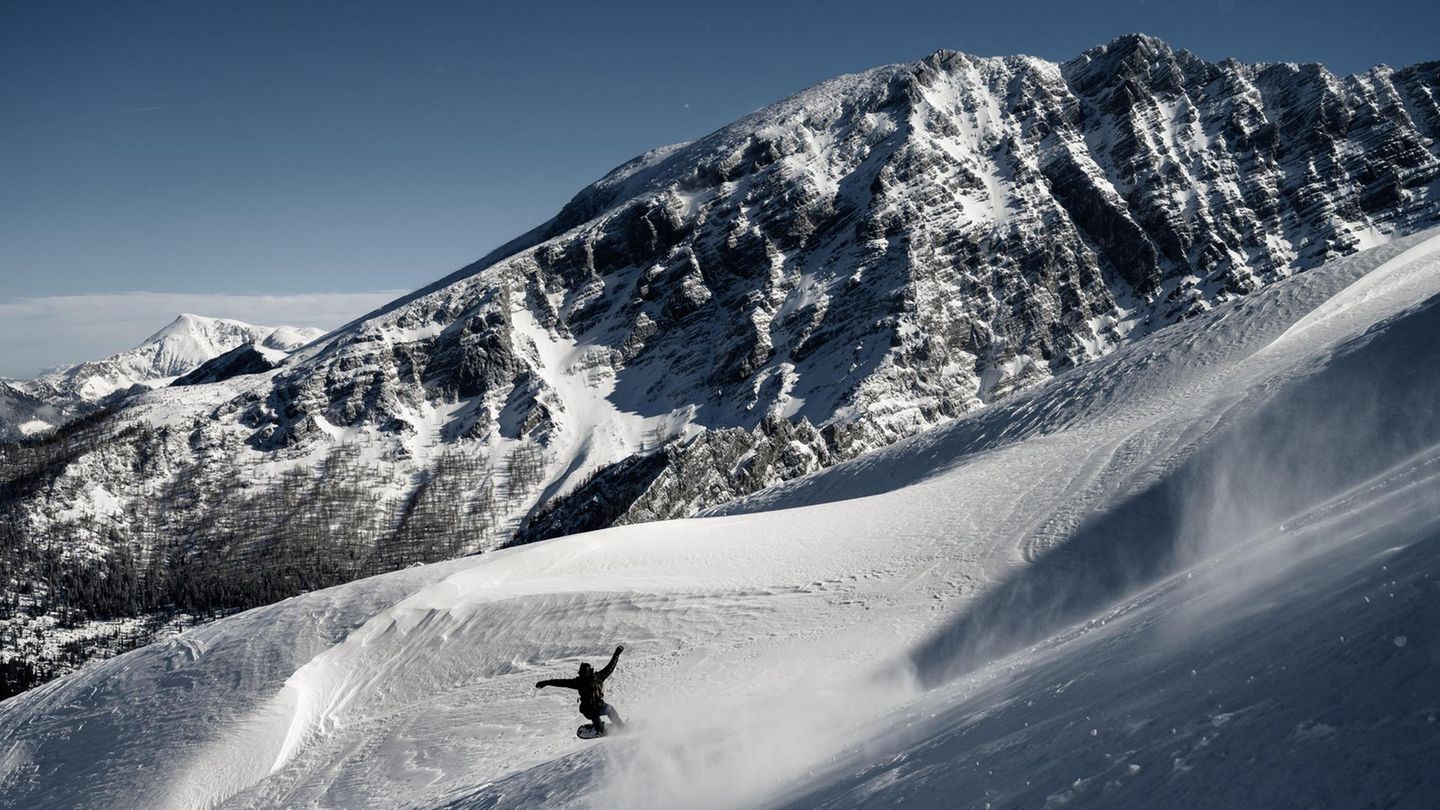 Watzmann im Winter: Ein Snowboader fährt über die tiefverschneiten Hänge der Hochalm. Gegenüber sind die Westwände des Watzmannstocks zu sehen.