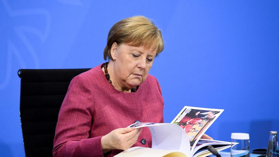 In altrosa Blazer sitzt Angela Merkel an einem Tisch vor einer blauen Wand und blättert in einem Fotobuch