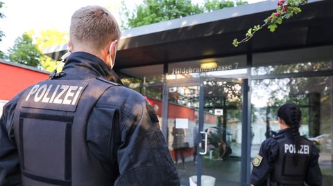 Ein blonder Polizist und eine dunkelhaarige Polizistin sind von hinten zu sehen, wie sie auf einen gläsernen Eingang zugehen