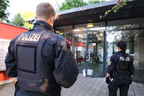 Ein blonder Polizist und eine dunkelhaarige Polizistin sind von hinten zu sehen, wie sie auf einen gläsernen Eingang zugehen