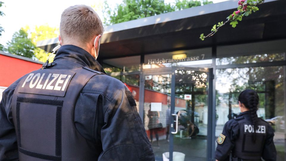 Ein blonder Polizist und eine dunkelhaarige Polizistin sind von hinten zu sehen, wie sie auf einen gläsernen Eingang zugehen