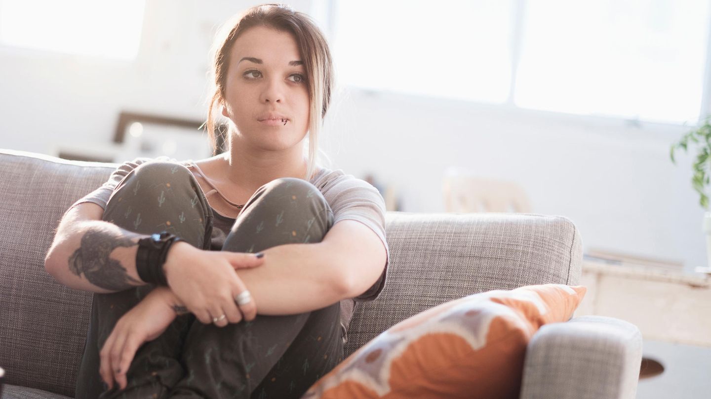 Eine junge Frau sitzt mit angezogenen Beinen auf dem Sofa