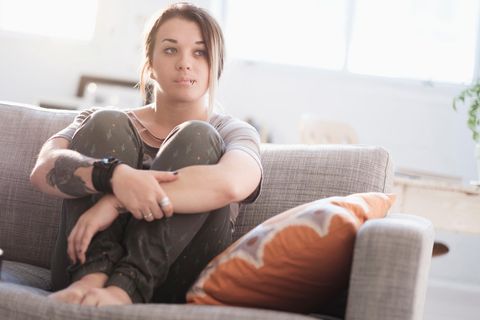 Eine junge Frau sitzt mit angezogenen Beinen auf dem Sofa