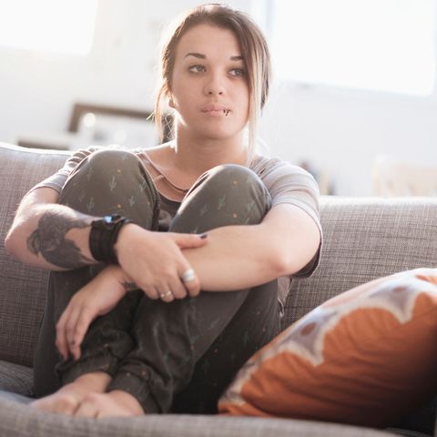 Eine junge Frau sitzt mit angezogenen Beinen auf dem Sofa