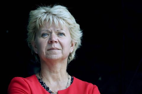 Eine weiße Frau mit hellblondem Bob und rotem Blazer schaut nachdenklich