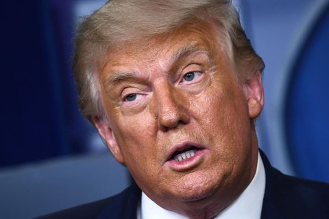 Mit schräg gelegtem Kopf spricht Donald Trump vor einer blauen Wand