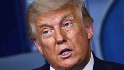 Mit schräg gelegtem Kopf spricht Donald Trump vor einer blauen Wand