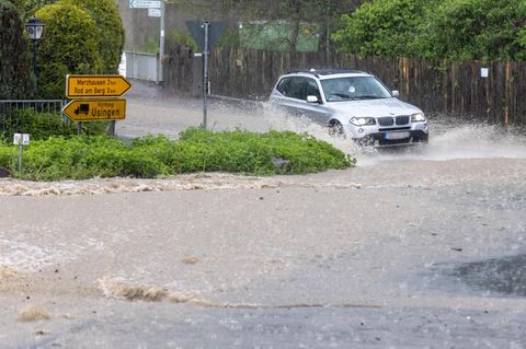 Ein Fahrzeug fährt durch eine Straße, die nach einem starken Gewitter überflutet ist
