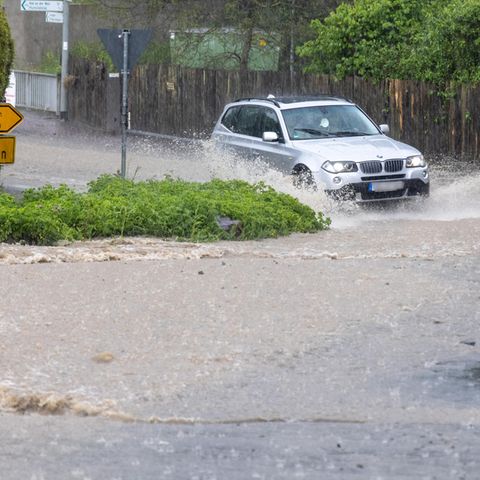 Ein Fahrzeug fährt durch eine Straße, die nach einem starken Gewitter überflutet ist