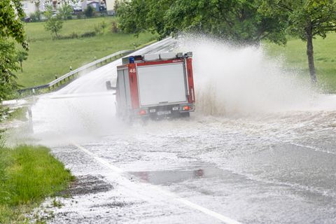Ein Fahrzeug der Feuerwehr fährt im Ortsteil Brombach auf einer Straße, die nach einem starken Gewitter überflutet ist.