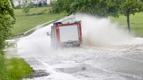 Ein Fahrzeug der Feuerwehr fährt im Ortsteil Brombach auf einer Straße, die nach einem starken Gewitter überflutet ist.