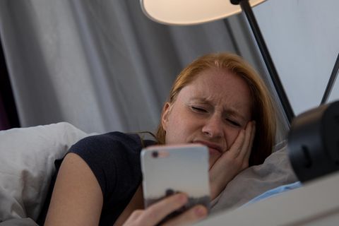 Eine Frau wacht auf und schaut müde auf den Wecker
