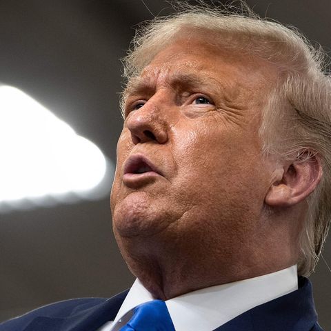 Donald Trump Trump schaut in die Höhe, neben ihm eine helle quadratische Denkenleuchte
