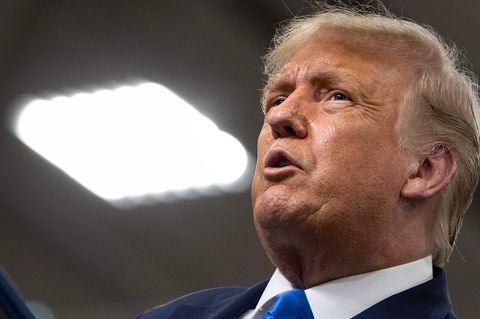 Donald Trump Trump schaut in die Höhe, neben ihm eine helle quadratische Denkenleuchte