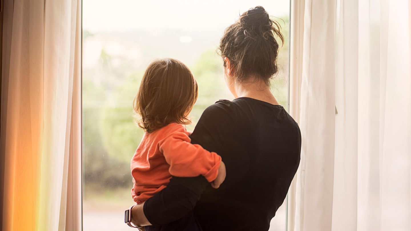 Frau trägt Kleinkind auf dem Arm und schaut aus dem Fenster