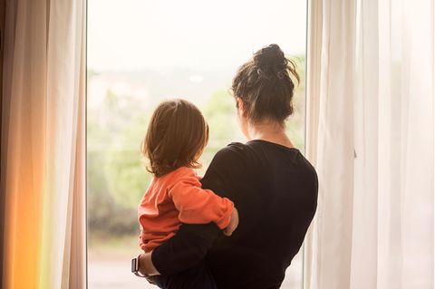 Frau trägt Kleinkind auf dem Arm und schaut aus dem Fenster