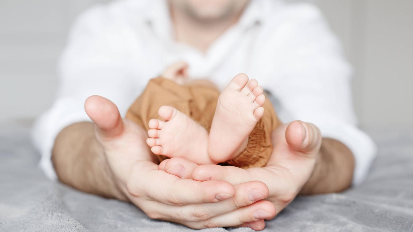 Die kleinen Füße eines kleinwüchsigen Babys in den Händen eines Erwachsenen