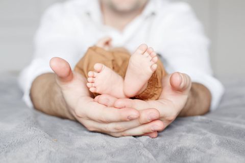 Die kleinen Füße eines kleinwüchsigen Babys in den Händen eines Erwachsenen