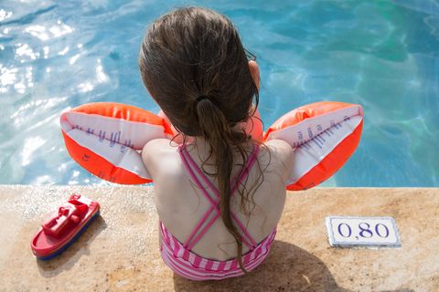 Ein kleine Mädchen sitzt mit Schwimmflügeln am Beckenrand