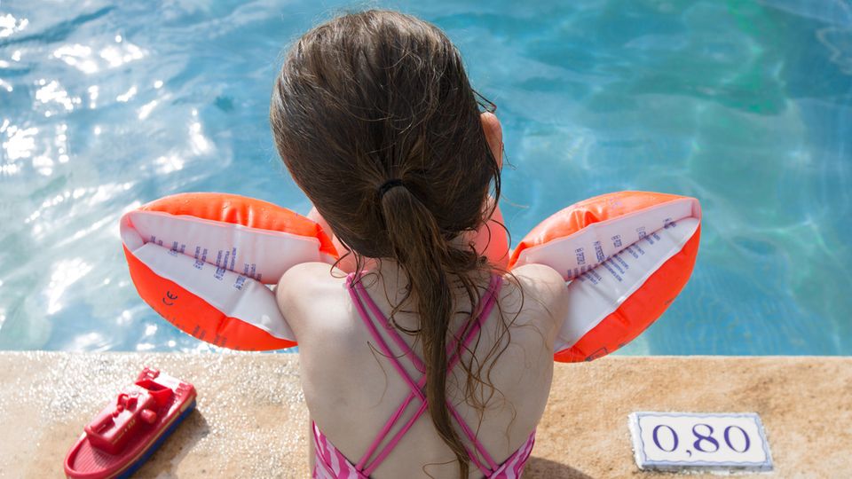Ein kleine Mädchen sitzt mit Schwimmflügeln am Beckenrand