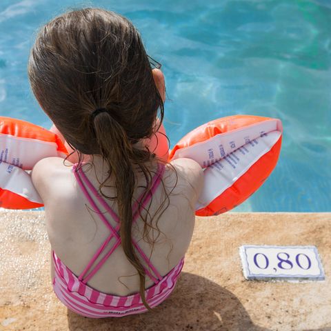 Ein kleine Mädchen sitzt mit Schwimmflügeln am Beckenrand
