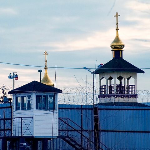 Ein weißes Wachhäuschen steht vor einem blauen Wellblechzaun mit Stacheldrahtrollen darauf
