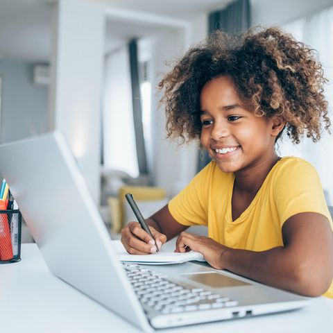 Mädchen sitzt vor ihrem Laptop und schreibt sich Sachen auf einen Collegeblock