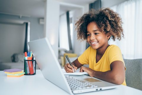 Mädchen sitzt vor ihrem Laptop und schreibt sich Sachen auf einen Collegeblock