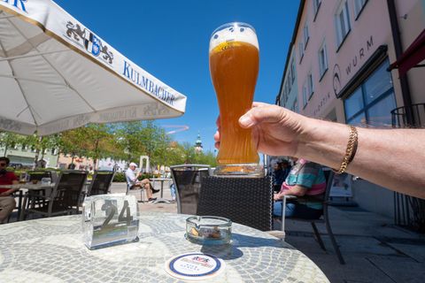 Ein Mann hält ein Glas mit Weißbier im Außenbereich von einer Eisdiele hoch