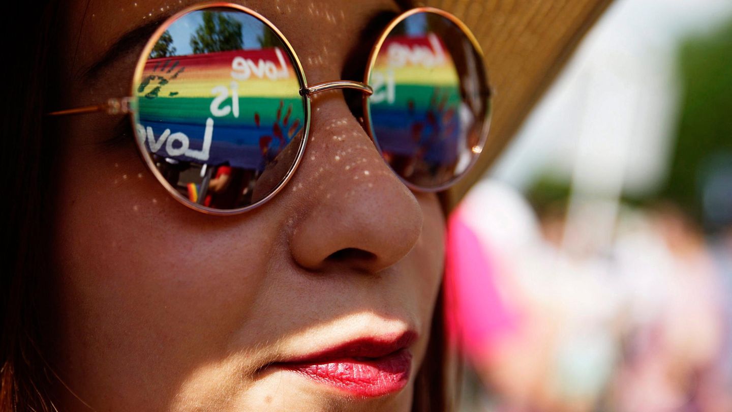 Eine Frau trägt eine Sonnenbrille, in der sich Regenbogenfarben spiegeln
