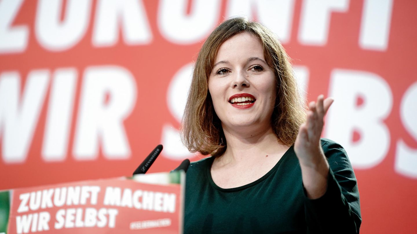 Eine junge Frau mit schulterlangen Haaren hält eine Rede vor einer roten Wand mit weißer Schrift "Zukunft machen wir selbst"