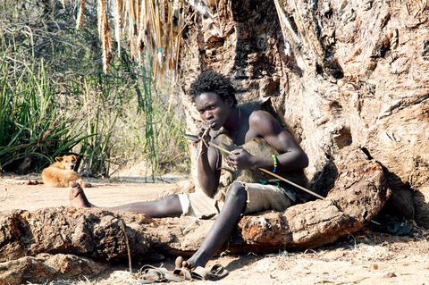 Ein junger Mann vom Volk der Hadza fertigt einen Bogen