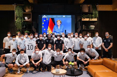 Toni Kroos hält ein Trikot mit dem Nachnamen von Kanzlerin Merkel hoch, er und das restliche Team posieren für ein Foto