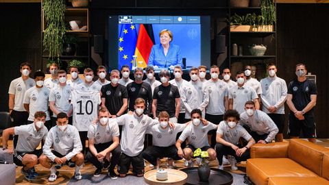 Toni Kroos hält ein Trikot mit dem Nachnamen von Kanzlerin Merkel hoch, er und das restliche Team posieren für ein Foto