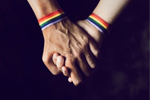 Zwei Männer mit regenbogenfarbigen Armbändern halten Händchen