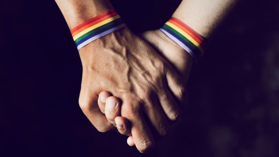 Zwei Männer mit regenbogenfarbigen Armbändern halten Händchen