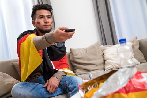 Ein in den Farben der deutschen Nationalmannschaft gekleideter Mann verfolgt ein Fußballspiel am Fernseher (gestellte Szene)