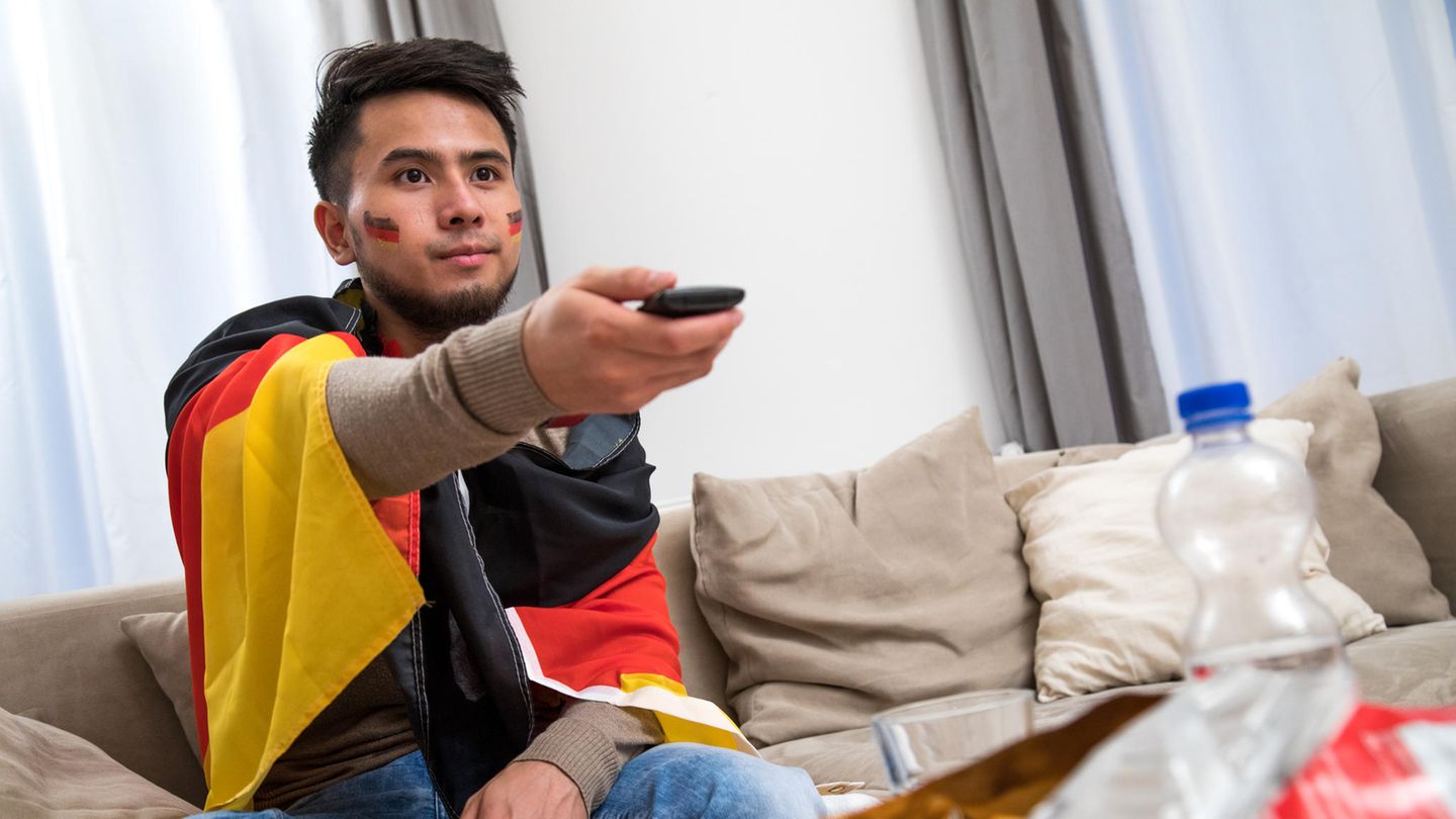 Ein in den Farben der deutschen Nationalmannschaft gekleideter Mann verfolgt ein Fußballspiel am Fernseher (gestellte Szene)