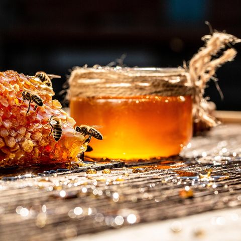 Bienen sind an Honigwaben zugange. Im Hintergrund steht ein Glas mit Honig.