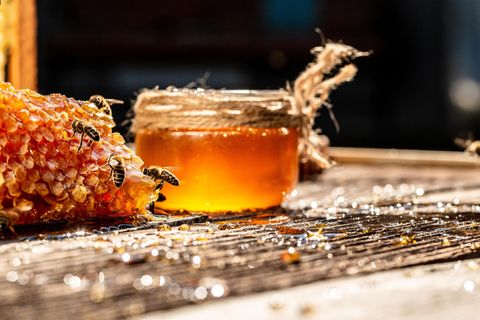 Bienen sind an Honigwaben zugange. Im Hintergrund steht ein Glas mit Honig.
