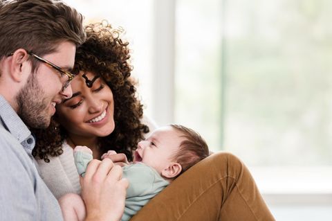 Ein Baby liegt auf den Beinen seines Vater uns strahlt