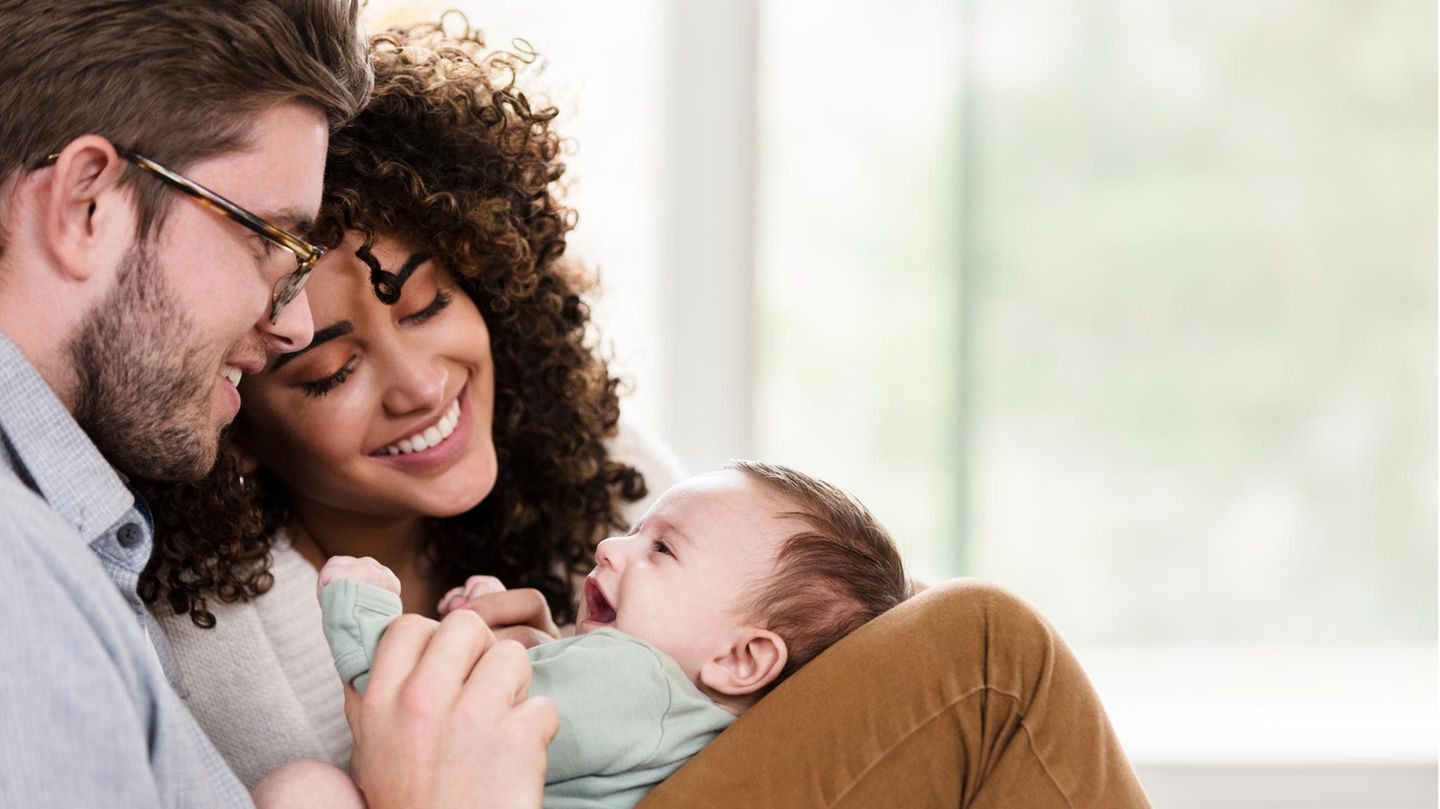 Ein Baby liegt auf den Beinen seines Vater uns strahlt