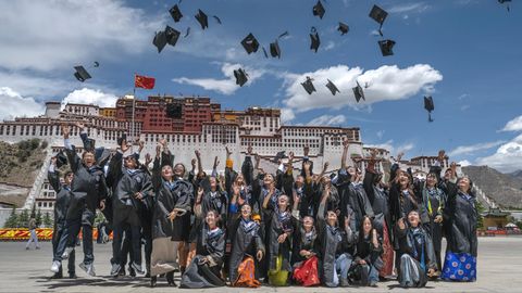 Heile Welt mit hochfliegenden Hüten der Studierenden in Lhasa mit dem Potala-Palast im Hintergrund.